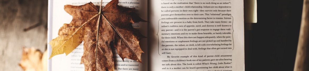 A book is open, and a passage marked with a pencil. A yellow post-it note sticks out the side. One the left-hand page, a large yellowy-brown sycamore leaf is spread out.